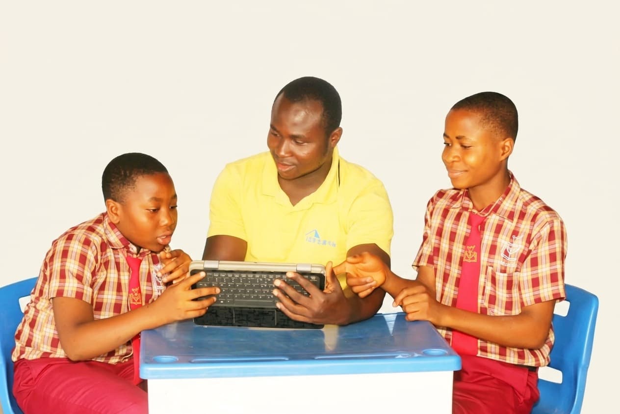 A teacher guiding two students through a lesson on a laptop